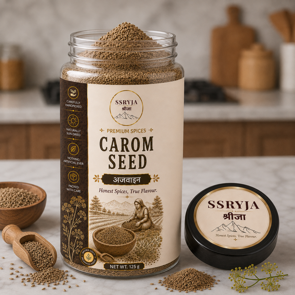 A jar of SSRYJA Carom Seed spice mix is shown on a marble surface with a small wooden scoop, loose seeds, and a separate black lid in the foreground. The background is a softly blurred kitchen setting.
