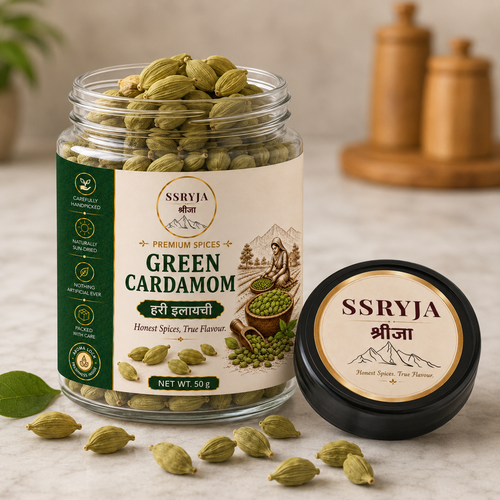A jar of SSRYJA Green Cardamom spices with its black lid placed beside it on a light stone surface. The clear jar shows green cardamom pods inside, and the cream-colored label includes product details and illustrations.