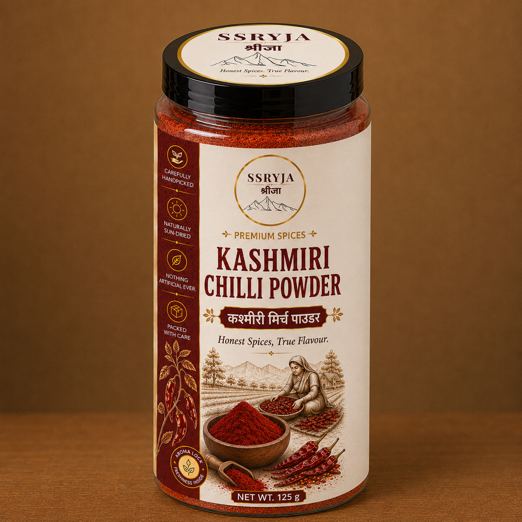 A jar of SSRYJA Kashmiri Chilli Powder on a brown background. The jar has a cream-colored label with red and black text, showing illustrations of chili peppers and a person grinding spices.